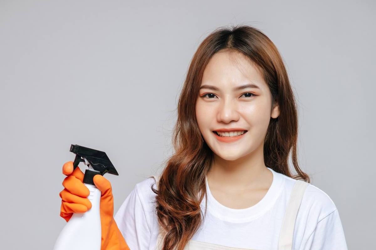 Cleaner in an apron and rubber gloves holding cleaning supplies