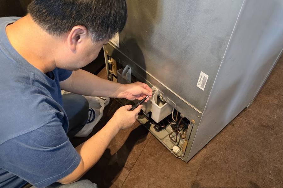 Technician fixing parts at the back of a fridge by AC Saviour Engineering