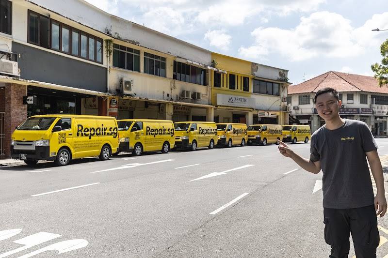 Staff member beside a row of branded service vans by Repair.sg