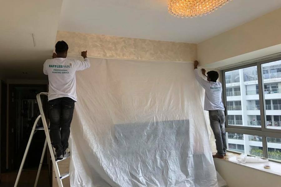 Painters covering a wall with plastic sheeting before painting by Stamford Painters
