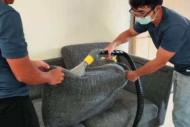 Two staff cleaning a fabric sofa cushion with an extraction tool by CasperCleanSG
