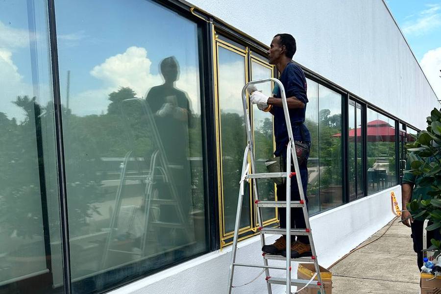 Technician on a ladder working on a building's glass windows by Well Handled Development